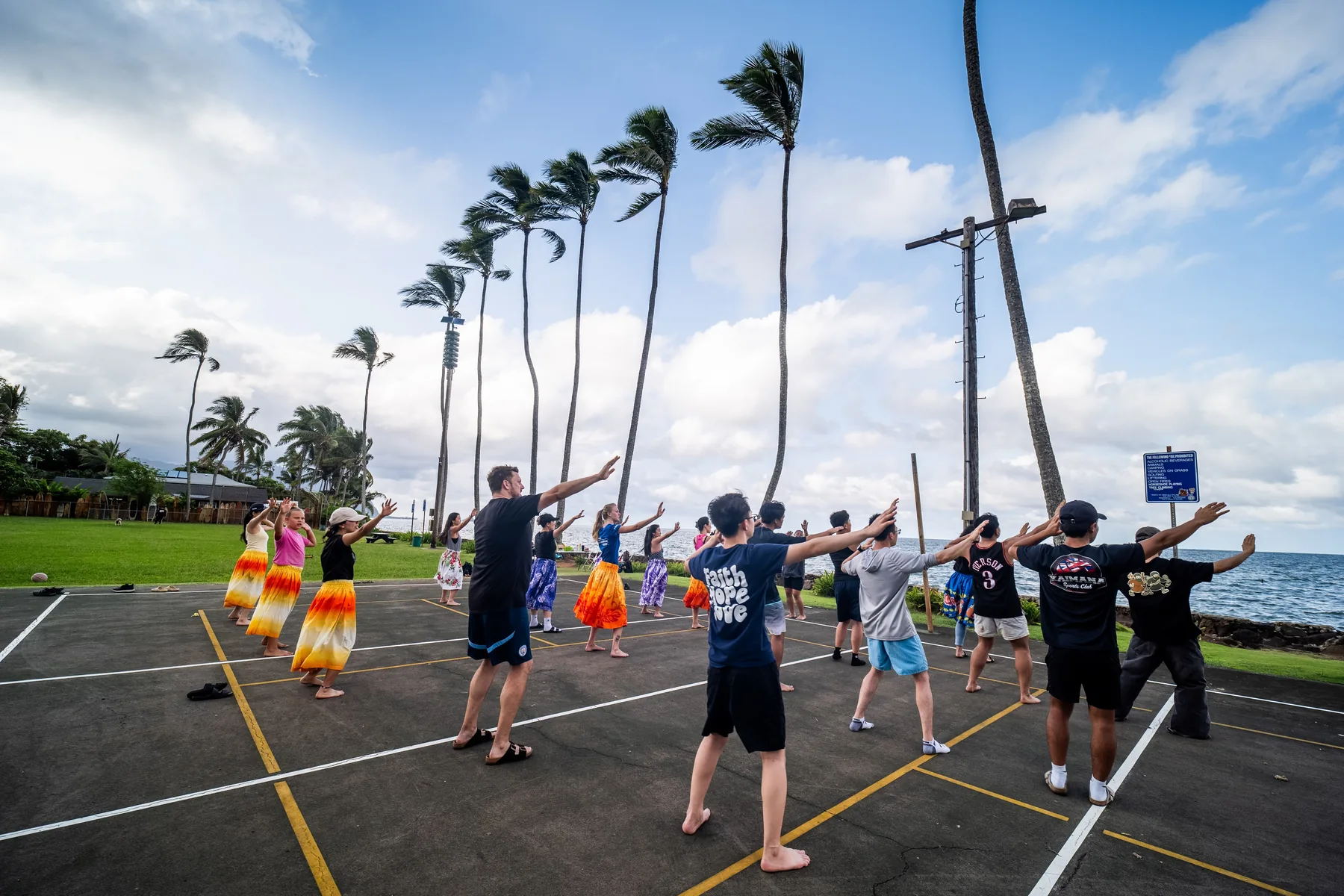 Team members practicing hula near palm trees and the ocean.