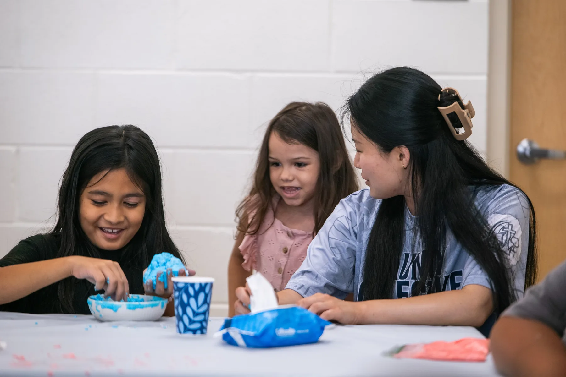 Team member helping children mix colorful slime at a table.