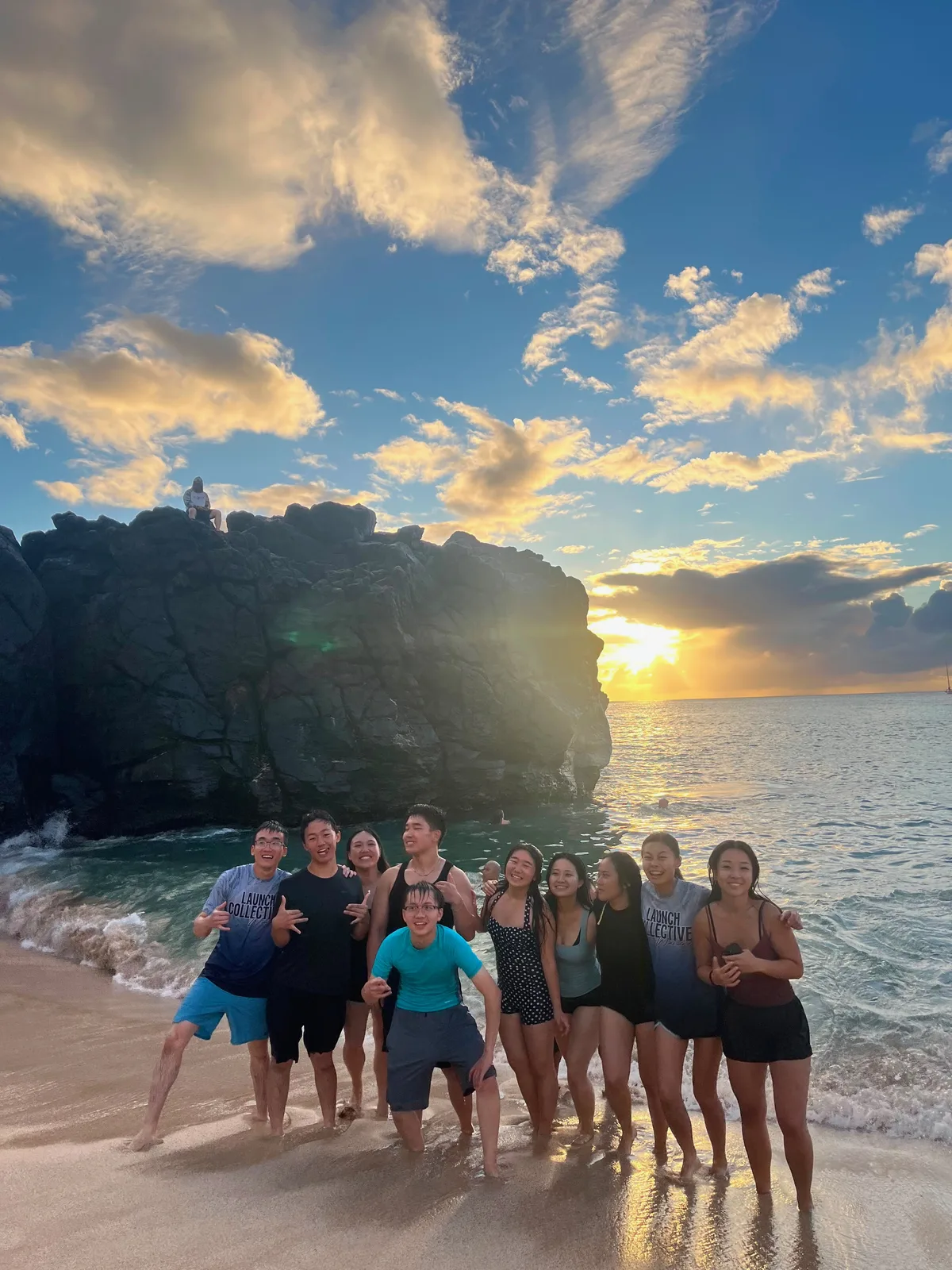 Team standing in the surf at Waimea Bay with the sunset behind the rock.